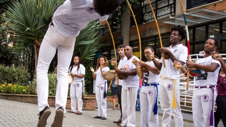 Capoeirista salta em uma roda de rua acompanhada por berimbaus
