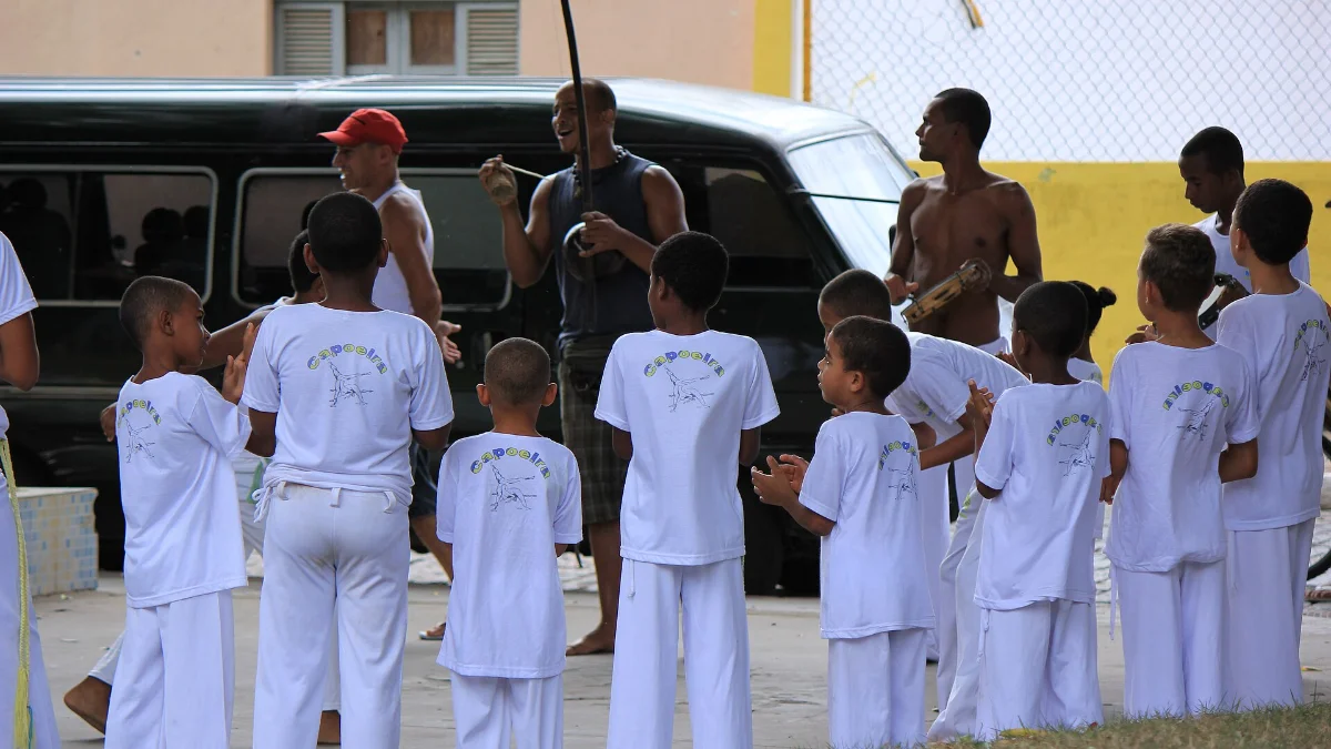 Crianças de uniforme branco batem palmas em roda de capoeira com berimbau e pandeiro em Cachoeira, Bahia