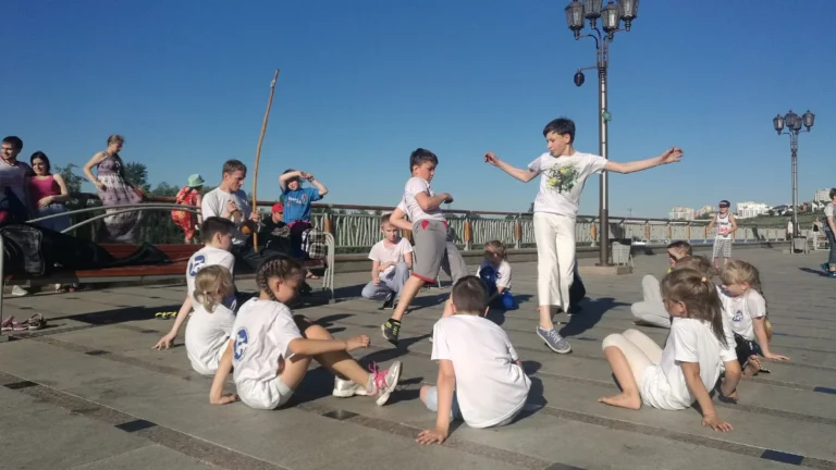 Crianças em uma roda de capoeira ao ar livre, com berimbau e jogo no centro